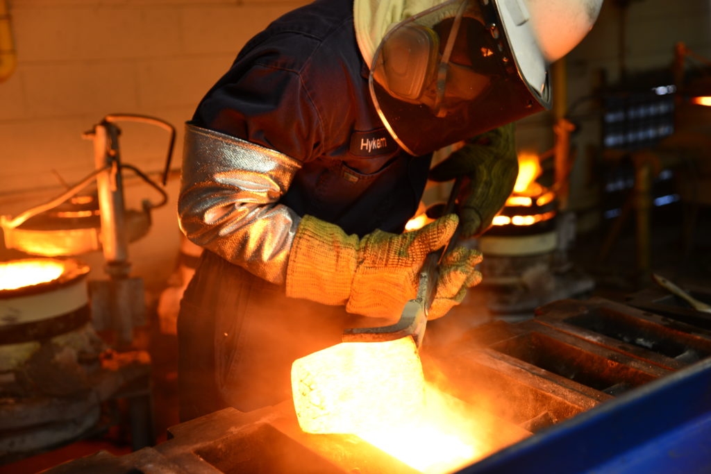 A melter pouring molten precious metals into a cast.