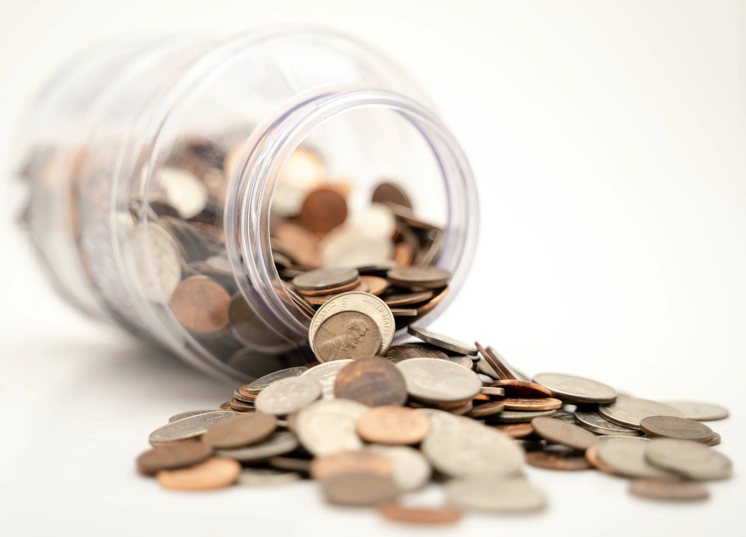 A jar laying on its side with various coins spilling out