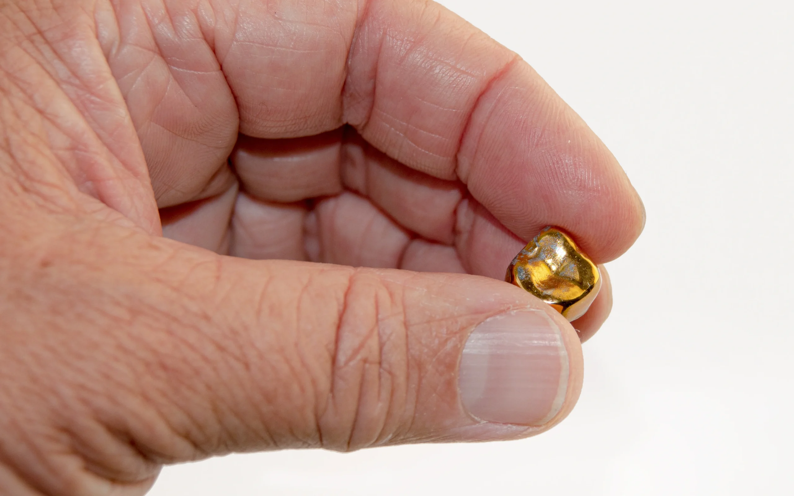 A hand holding a single gold crown tooth implant