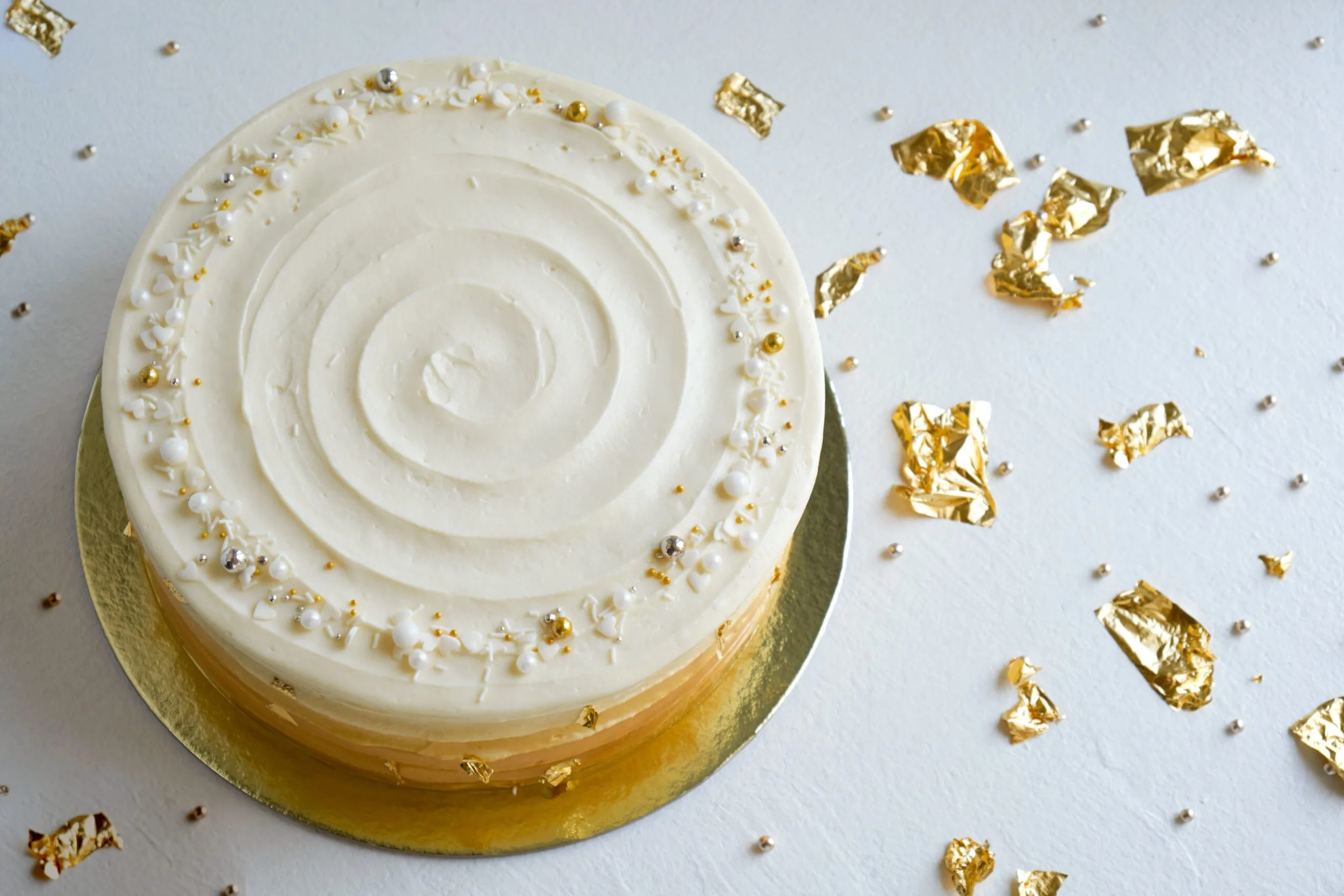 Cake with white cream, decorated with silver and gold confectionery sprinkles and gold leaf.