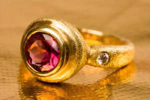 Gold ring with pink gem on golden background.